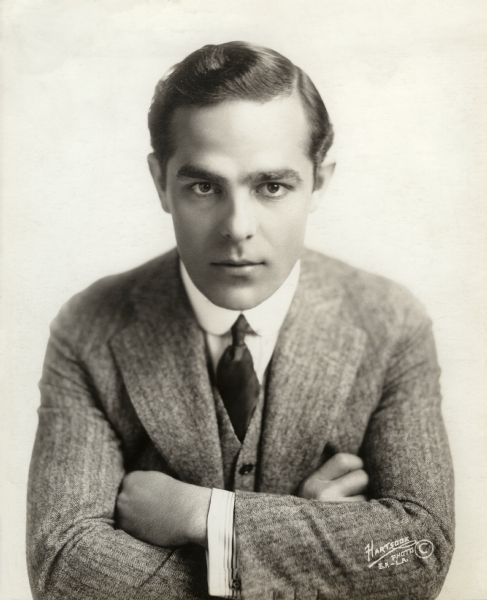 Head and shoulders studio publicity portrait of silent film star Antonio Moreno in a narrow herringbone worsted wool coat and waistcoat, dark necktie, and small detachable collar with rounded points.