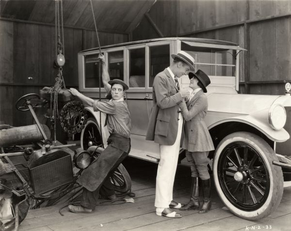 Buster Keaton hoists a Model T engine from a wrecked car as Virginia Fox flirts with an unidentified actor in a scene still for the 1922 comedy short "The Blacksmith."