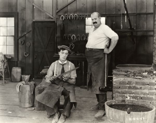 The blacksmith's assistant (played by Buster Keaton) files his nails as his employer (Joe Roberts) looms over him in a scene still from the 1922 silent comedy "The Blacksmith."
