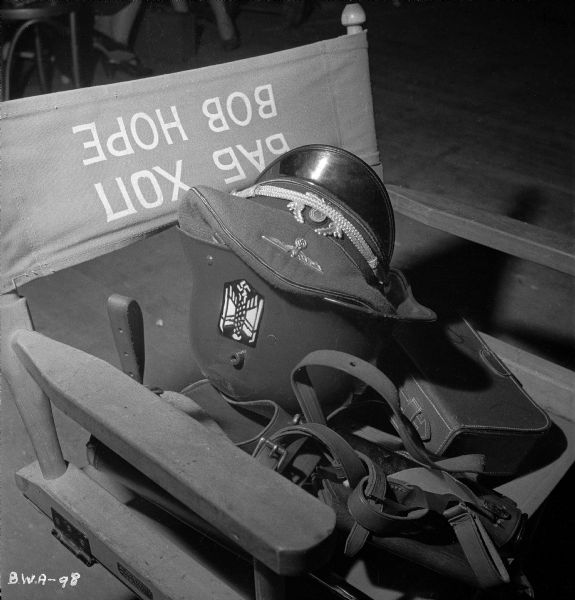 Production still with costume and "Bob Hope" director's chair A German army steel helmet and officer's visor cap rest on a director's chair that has been amusingly stenciled with two versions of the name "Bob Hope," one in reversed Latin letters and the other in up-side-down Cyrillic.