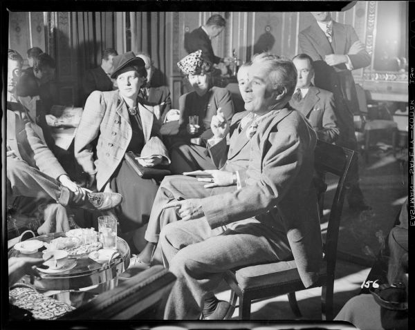 Charlie Chaplin talking to eight or more reporters sitting around him in a meeting room at the Waldorf Astoria in New York.