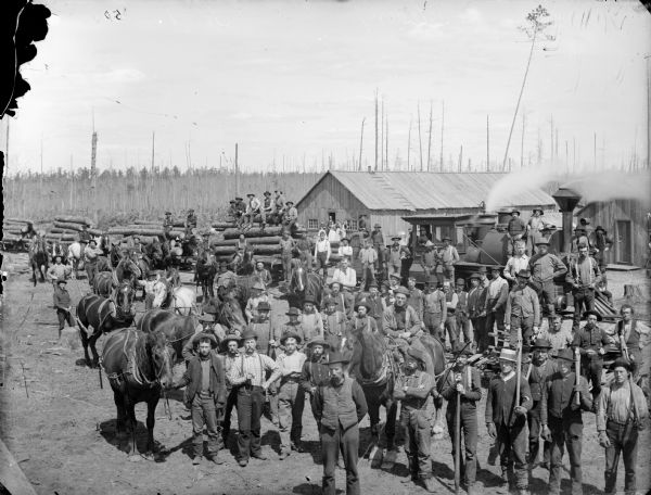 Elevated view of lumber camp with loggers posing in front of a train loaded with logs.
