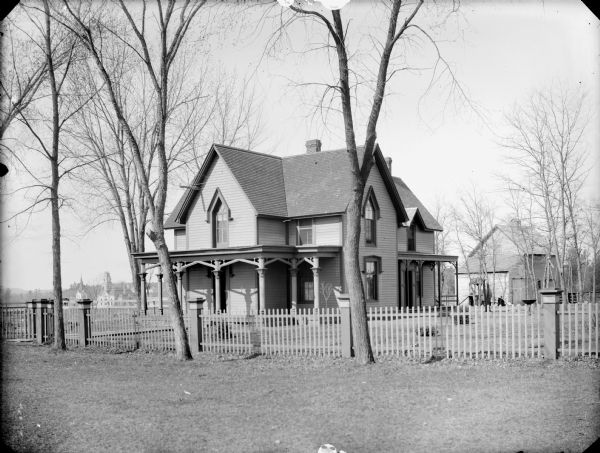 Two-story wooden frame house surrounded by a picket fence. In the far background is the Jackson County Courthouse, possibly the Caves House.	
