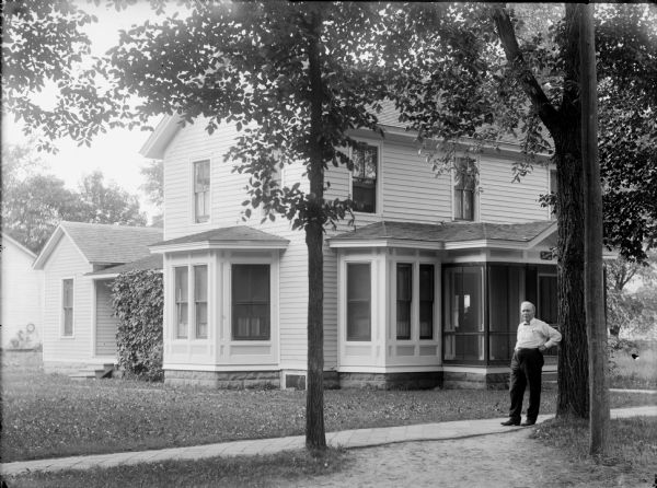 Man posed standing on a board sidewalk in front of a two-story frame house. Probably Dr. L.P. Gaillardet in front of the Darnell House, which was later moved to make a parking lot for the Methodist Episcopal Church.	Dr. Gaillardet's name is on a sign above the front door.