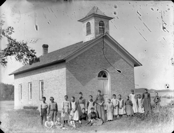 Group portrait of a woman and a group of boys and girls posing standing in front of a brick building, probably a school group, possibly the Everett School in Garden Valley.	