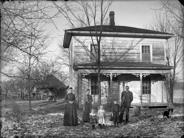 People in front of Frame House Two women, three girls, and a man posing standing in the yard in front of a two-story frame house.