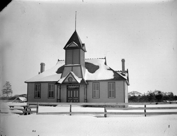 Pleasant View School, Brockway, Wisconsin View across snow-covered ground towards a fence in front of a wooden school house building. Identified as the Pleasant View school in Brockway.