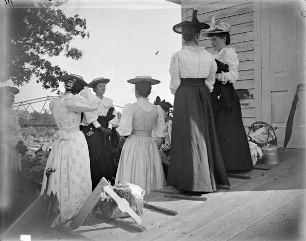Group of Women Outdoor view of seven women posing standing near or on a wooden porch with a bridge in the background.