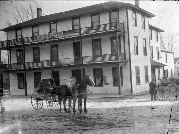 Merchant's Inn on a Rainy Day Exterior view of Merchant's Inn on a rainy day. Located at the southwest corner of S. First Street and Fillmore. A man in a buggy pulled by two horses in the street. Another man standing next to a wagon on the right.