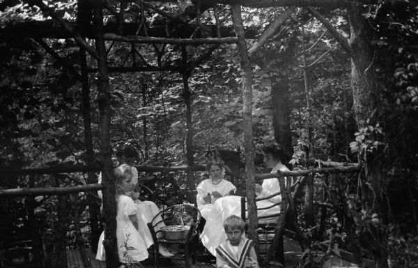The photographer's wife, Clothilde, far right, and children, from left, Margaret, Alice, Helen, and Ferdinand Leonard, in a rustic gazebo on the grounds of their home. Clothilde and the two older girls are shelling peas.