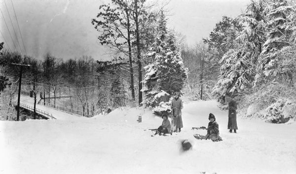 The photographer's four children pose with their sleds near Sheridan Road. There is a bridge over a ravine in the background and a blurred image of a dog in the foreground.