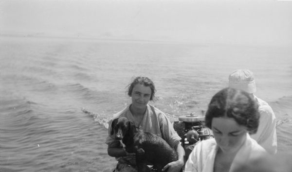 Helen Hotz Schmid holds a wet dachsund while riding in a motorboat with other family members.  Her brother, Ferdinand L. (Fedy) Hotz mans the Evinrude motor.