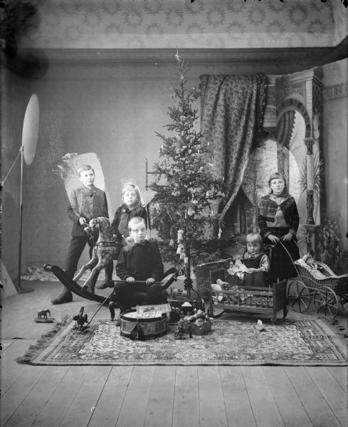 Studio portrait of Gerhard Gesell's five children (l to r: Arnold, Bertha, Robert, Gerhard, and Wilma) posed around a Christmas tree with their gifts.