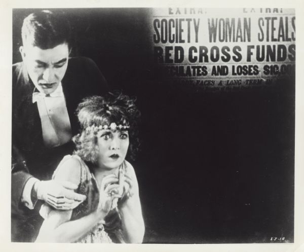A menacing Sessu Hayakawa looms over a terrified Fannie Ward in a scene from the silent film "The Cheat" (Paramount 1915). In the upper right hand corner, an iris close-up reveals a newspaper headline: "Society Woman Steals Red Cross Funds."