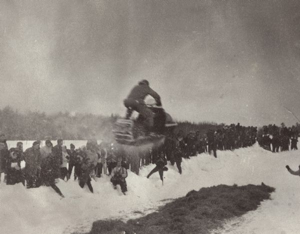 A snowmobile rider long-jumps at the Eagle River Snowmobile Derby. According to the notes in the photograph album, this was the "world record long jump." Two of the competitors broke their legs during the 1969 event and it was thereafter discontinued for many years.