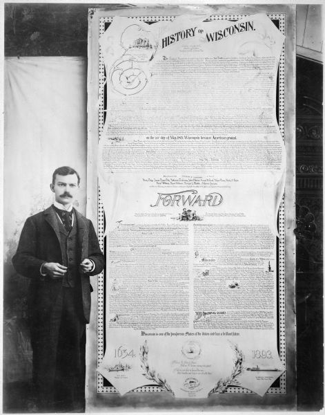 John Fawcett Tyrrell, handwriting expert and documents examiner of Milwaukee, standing at left of an illuminated poster, ten feet high, entitled "The History of Wisconsin" and entirely handwritten by him. He is wearing a suit and appears to be holding a pen. He was born in Australia in 1861 and came to the United States as a boy. As a young man, he was employed by the Northwestern Mutual Life Insurance Company. He remained an employee there for forty-five years. He became an expert engrosser and was soon turning out some of the finest penmanship seen in the country.