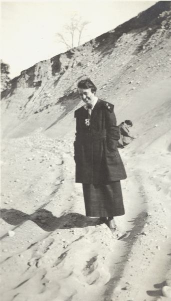 Women in a Sand Pit Florance Trask poses standing in a sand pit located near the intersection of Fish Hatchery Road and Park Street. Another woman, Grace, can be seen digging in the sand behind her. A note on the back of the photograph reads, "Pieh's Hill, Keyes Hill."