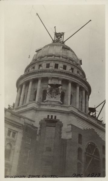 Scaffolding Used to Build the Wisconsin State Capitol View from ground looking up at the scaffolding and cranes on the Wisconsin State Capitol used to construct the building. Text at bottom reads: "Wisconsin State Capitol — Dec 1913."