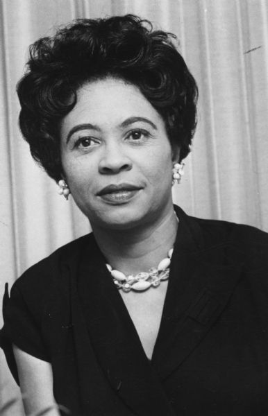 Portrait of Daisy Bates wearing a dark dress and beaded earrings and necklace.