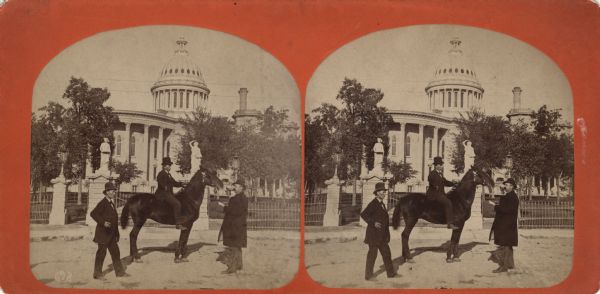 Stereograph. This view from East Washington Avenue shows photographer Andrew Dahl on his horse "Curnel" in front of the Wisconsin State Capitol. Dahl had just returned from the Centennial Exposition in Philadelphia. Two other men are standing near the horse.