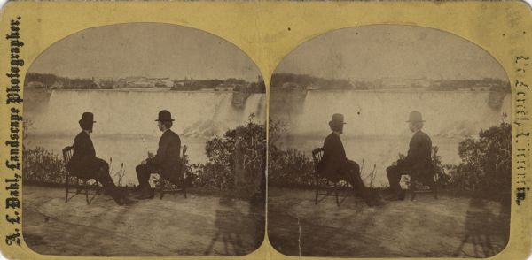 Stereograph of "Two different views of the Falls from Canada side," from the series "Niagara Falls and Suspension Bridge" as mentioned in Dahl's 1877 "Catalogue of Stereoscopic Views." Two men are sitting in wooden chairs as they gaze at the falls, quite close to the edge. Note the shadow of the photographer and camera in the right foreground.
