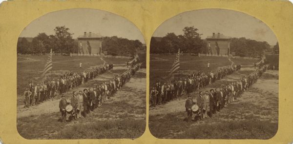 Outdoor elevated view of a reunion of the Norwegian American men of the 15th Regiment of the Wisconsin Volunteer Infantry at Luther College. They are posing in two lines holding the American flag and the Norwegian flag.
