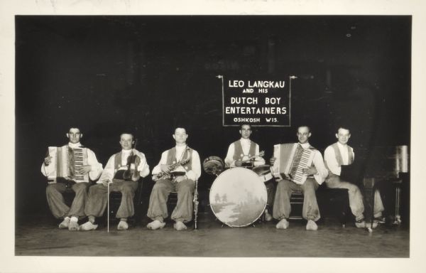 Photograph submitted to the state of Wisconsin for trademark registration. Group portrait of the six men in Dutch costume and wooden shoes holding musical instruments. A sign in the center reads: Leo Langkau and the Dutch Boy Entertainers, Oshkosh, Wis."