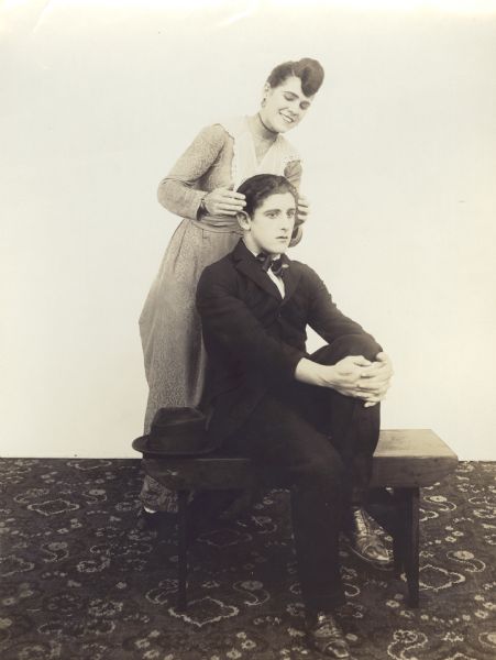 Film still - interior - actress and actor standing together; no set beyond carpet on the floor.