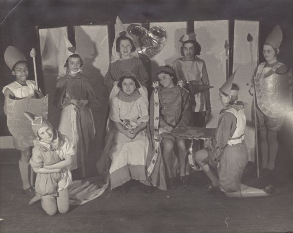 Image from the Tansy Camp Fire Girls album, with cast members of the Queen of Hearts play: Armida Peterson, Rose Martinelli (lady-in-waiting), Rosalyn Schiavo (lady-in-waiting), Sara Parisi (herald), Iona Brantmeyer, Dorothy Pertzborn (knave), Mary Fedele (queen), Annie Falci (king), and Edna Lang (guard captain), posing on the set.