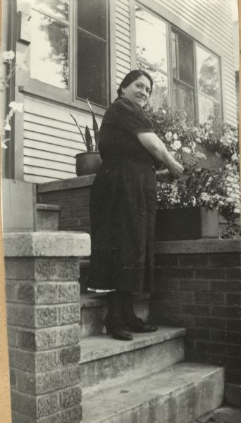 Neighborhood House Scrapbook: Garden Club Member Full-length view of a Neighborhood House Garden Club member standing on the front steps of her house and tending to her flower boxes while turning to face the camera.
