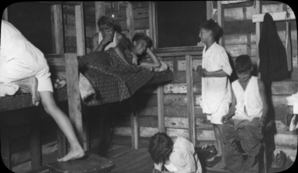 Neighborhood House: Boys at The Roost Group of boys getting ready for bed in a corner of The Roost in Piper's Woods (a 10 acre woods located a mile and a half past Forest Hill cemetery on the Speedway Road): one boy is climbing into his bunk with the aid of a chair; another boy is lying in his bunk with his head propped up on his arm and smiling and chatting with bunk mates who are changing for bed. The settlement house offered a number of summer camps for children. The Roost was built by Boy Scout Troops 22 (Neighborhood House) and 33 (Lowell School) beginning in 1928 and dedicated in 1931.