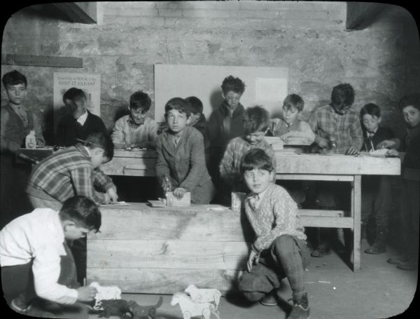Boys working on various stages of woodwork projects, with two boys in the foreground kneeling by some wooden toy animals with jointed limbs. The settlement house sponsored various craft activities for children.