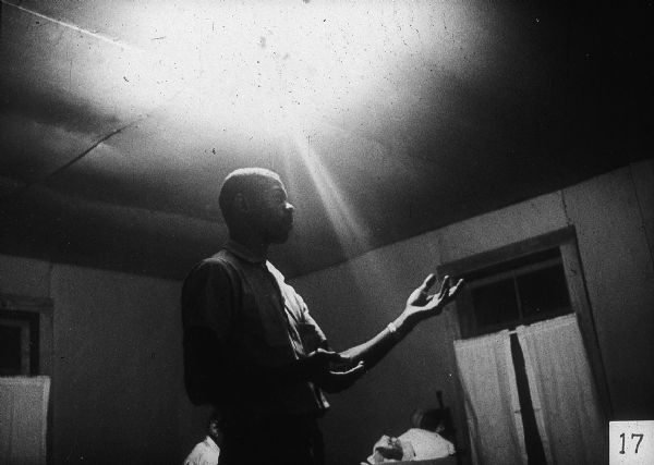 A man gestures with both hands, lit from above.