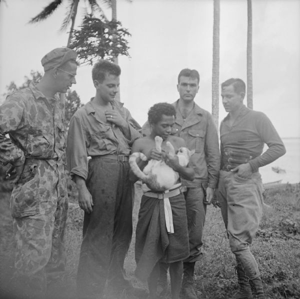 Four soldiers from Wisconsin look at a cat held by an indigenous man on Kiriwina Island in the Solomon Sea, New Guinea (present day Papua New Guinea). Names, left to right, Private Stanley Garncarz of Milwaukee, Private Jack Buth of Milwaukee, Isayah Momoivalu (with cat), Sergeant John Meier of Racine and Sergeant Morris Faust of Racine.