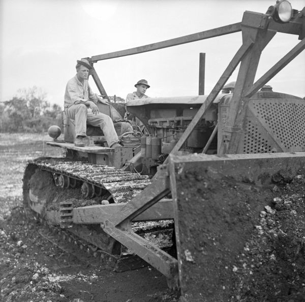 Corporal Eugene Cierzynski of Milwaukee, Wisconsin (left) instructs Corporal Edgar Hourscht of Trosky, Minnesota (right), on how to operate a D-8 Caterpillar bulldozer on Kiriwina Island in the Solomon Sea, New Guinea (present day Papua New Guinea). They are scooping up hard coral to create a revetment, a structure, sloped and formed to secure an area from artillery, bombing, or stored explosives.