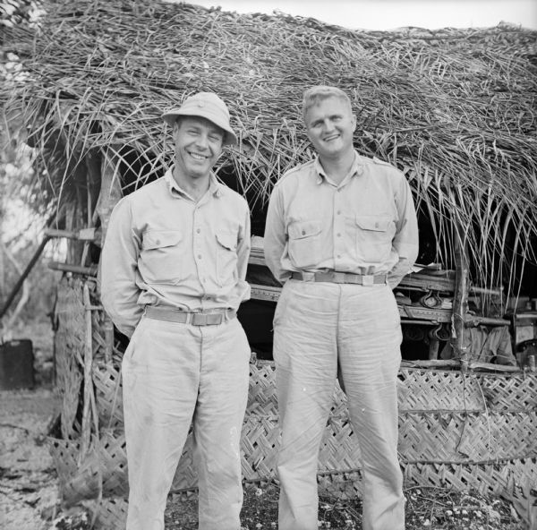 Major Howard Pagel (left) of Ladysmith, Wisconsin, and Captain Walter King (right) of Waco, Texas, stand together in front of the airfield aid station at the Kiriwina Airfield on Kiriwina Island in the Solomon Sea, New Guinea (present day Papua New Guinea).