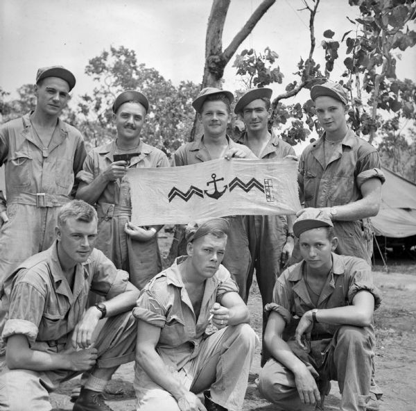 Wisconsin paratroopers in Port Moresby, New Guinea (present day Papua New Guinea), pose holding a captured Japanese marine banner and pistol they brought back after cutting off enemy soldiers trying to escape from Lae, New Guinea, in September. Soldiers' names, (standing from left) Captain Walter Lehmann of Hustisford, Sergeant Joseph Kellner of Marshfield, Corporal Arthur Smithback of Stoughton, Corporal Lloyd Heise of Oconto and Sergeant Kermit Brown of Greenwood, (kneeling from left) Raymond Barnowski of Monico, Sergeant Robert Miller of Marshfield and Private James McCann of La Crosse.
