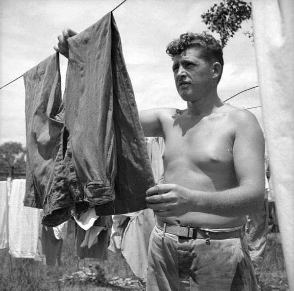 Corporal Jim Hiner of Lincoln Park, Michigan, hangs pants on a clothesline while on laundry duty at the Rough Raider Squadron Laundry, near Port Moresby, New Guinea (present day Papua New Guinea). More laundry can be seen behind him.
