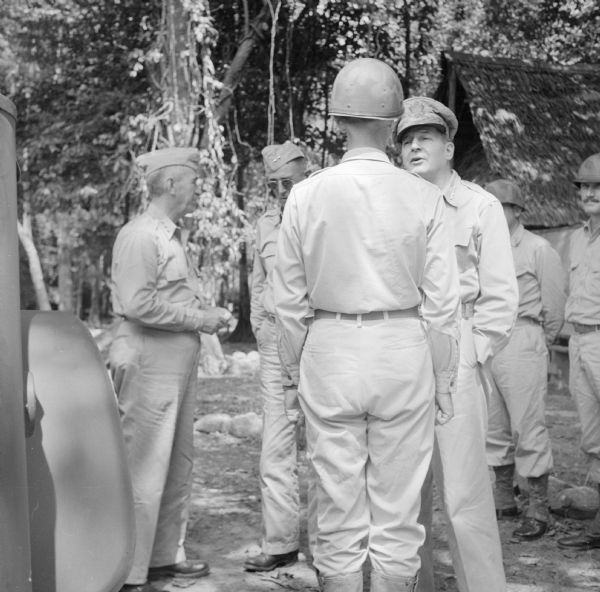 Four Star General Douglas MacArthur greets a soldier during a tour on Goodenough Island, in the Solomon Sea, New Guinea (present day Papua New Guinea). Other soldiers are standing in the background.
