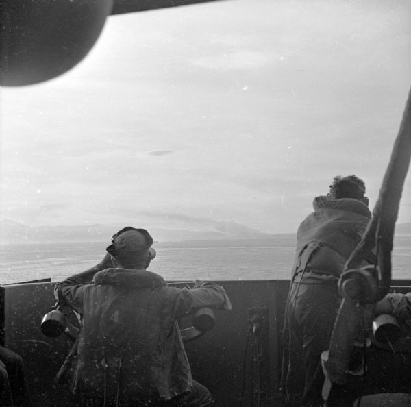 Seaman 2nd Class Jerry Burg (left) of Milwaukee, Wisconsin, and Seaman 2nd Class Harold Dawson of Toledo, Ohio, man the plane spotting station on an American cruiser off of Cape Gloucester while marines make their landing. Land and smoke are barely visible in the distance. Cape Gloucester was located in New Britain, New Guinea (present day Papua New Guinea).