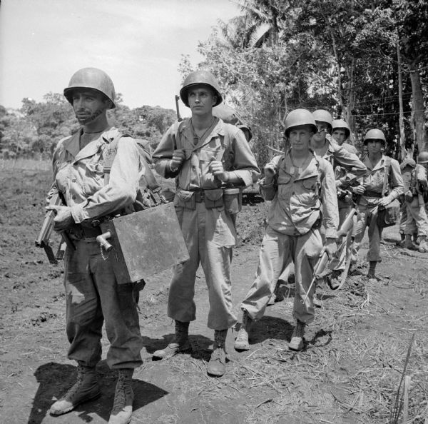 Artillery group leaving on patrol from camp in Saidor, New Guinea (present day Papua New Guinea). Names: (Front to rear) Private First Class Stanley Prachnaik of Hartford, Connecticut, Lieutenant Arnold Pettengill of Beacon, New York, Corporal Spurgeon Svihovec, Sergeant Glen Bateman, Private First Class Carl Krejci of Chippewa Falls, Wisconsin and Private First Class John Tyler of Bronson, Texas. They are wearing combat gear and carrying weapons and a radio.