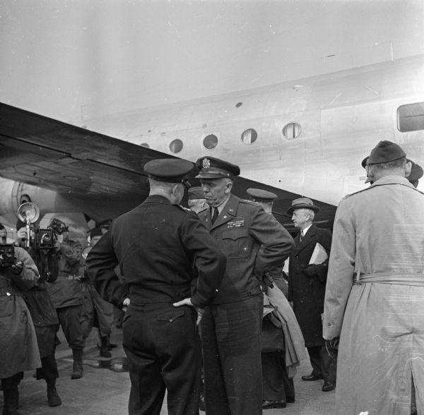 General Dwight D. Eisenhower speaks with General George C. Marshall at an airfield in Paris, France. The man behind Marshall's elbow is Senior Advisor to President Roosevelt, Justice James F. Byrnes. Several photographers are on the left. Robert Doyle notes: "Arrival of first plane US ATC (United States Air Transport Command) to fly direct from America today." The airplane is a Douglas C-54 Skymaster.