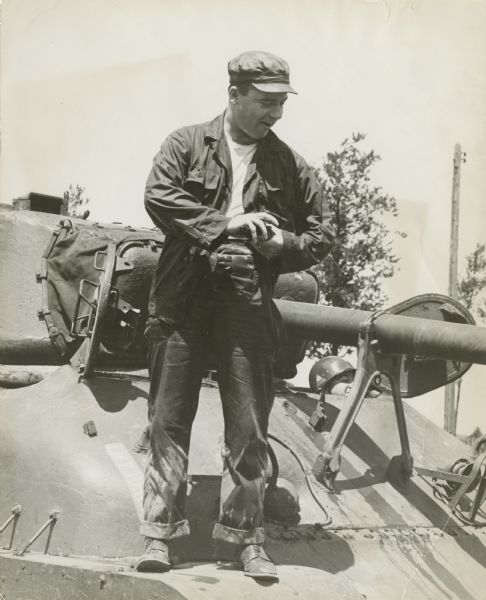Robert Doyle standing on a tank. A soldier is peering out of a hatch behind him on the right. A power pole and trees are in the background.