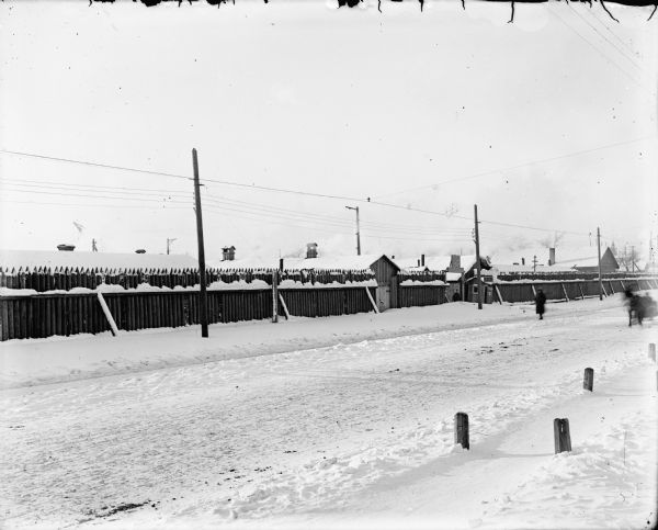U.S. Army Corps of Engineers Quarters View across snow covered road of the quarters of the 310th U.S. Army Corps of Engineers, Company C Quarters behind a timber fence. There are pedestrians in the road along with a horse-drawn vehicle. A man stands at the gate of the quarters, and a U.S. flag is painted on the sign above him.