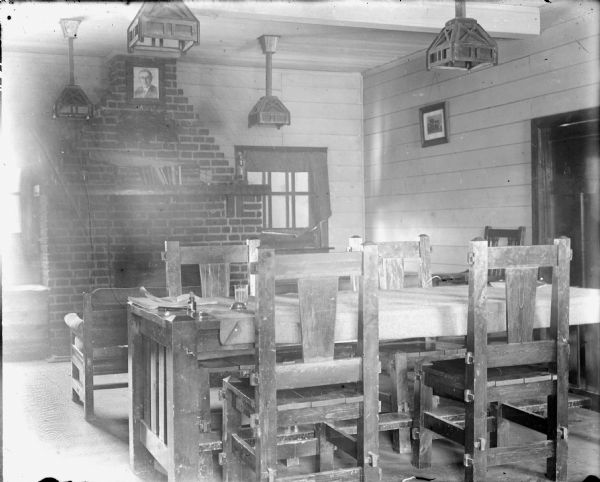 Officers Quarters, Interior Interior view of the officers quarters of the 310th United States Engineers. In the back of the room is a stone fireplace with a portrait of President Woodrow Wilson displayed at the top, and books on the mantel. There are stained glass ceiling lamps flanking the fireplace, and in the foreground is a wooden table and chairs.