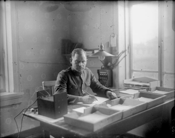 Seated portrait of Captain J.G. Morgan, Adjutant of the 310th United States Army Engineer Corps, in uniform at his desk. On his desk there appears to be a portable telephone with its receiver.