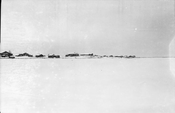 Village North of Pinega View across what is probably a frozen river covered with snow towards a village surrounded by a fence north of the Pinega settlement in northern Russia.