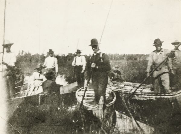 Group of men, with women passengers, poling canoes through a marshy stretch of water on the Brule River-St. Croix River portage between Lake Superior and the Mississippi River waterway.