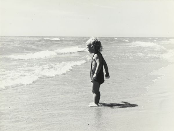 Small child standing on the shoreline of a sandy beach, looking out at  the waves, at Terry Andrae State Park on Lake Michigan.