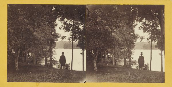 Man wearing "stove-pipe" hat, standing looking out over a lake.